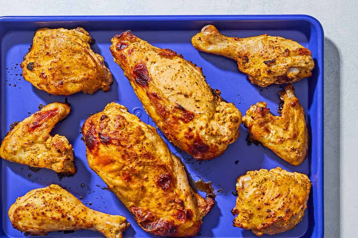 Pieces of cooked Greek yogurt marinated chicken on a sheet pan.