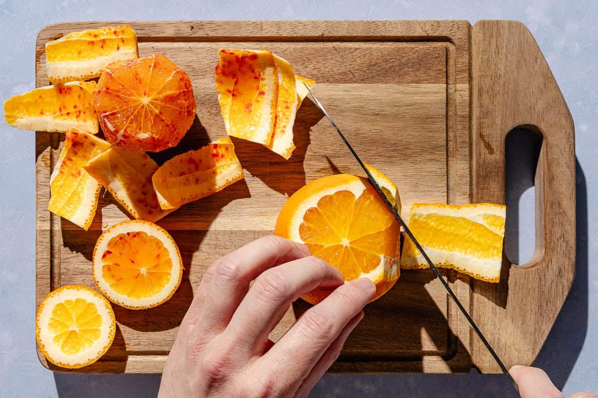 Two oranges on a cutting board in the process of having their peels slices off.