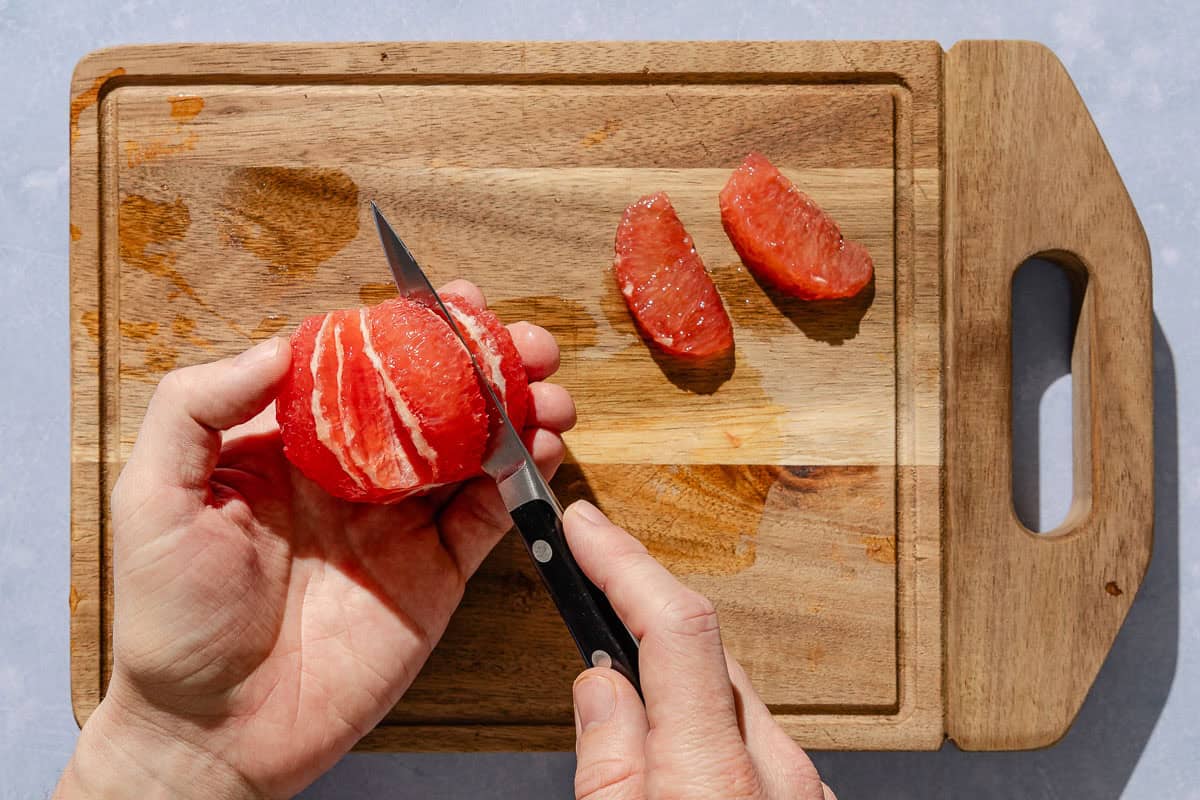 A peeled blood orange being sliced into wedges on a cutting board.