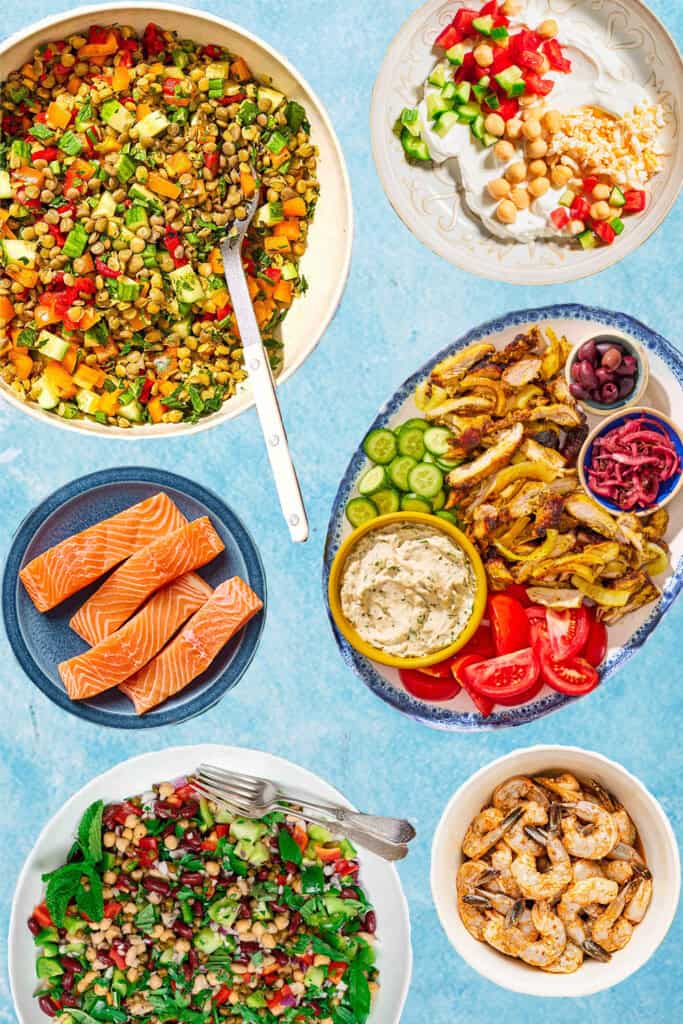 An image of various forms of essential Mediterranean diet proteins including bean and lentil salads, salmon, shrimp, chicken and yogurt.