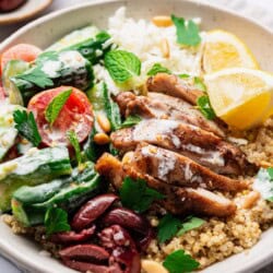 A quinoa chicken bowl on resting on a cloth napkin with a small bowl of kalamata olives nearby.