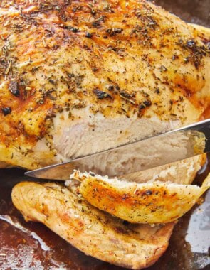 A roasted whole chicken being sliced with a knife.