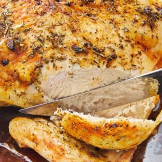 A roasted whole chicken being sliced with a knife.