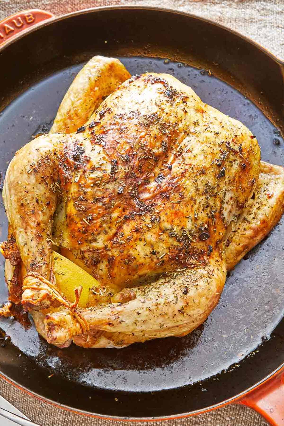 A roasted whole chicken rubbed in italian seasoning in a skillet.