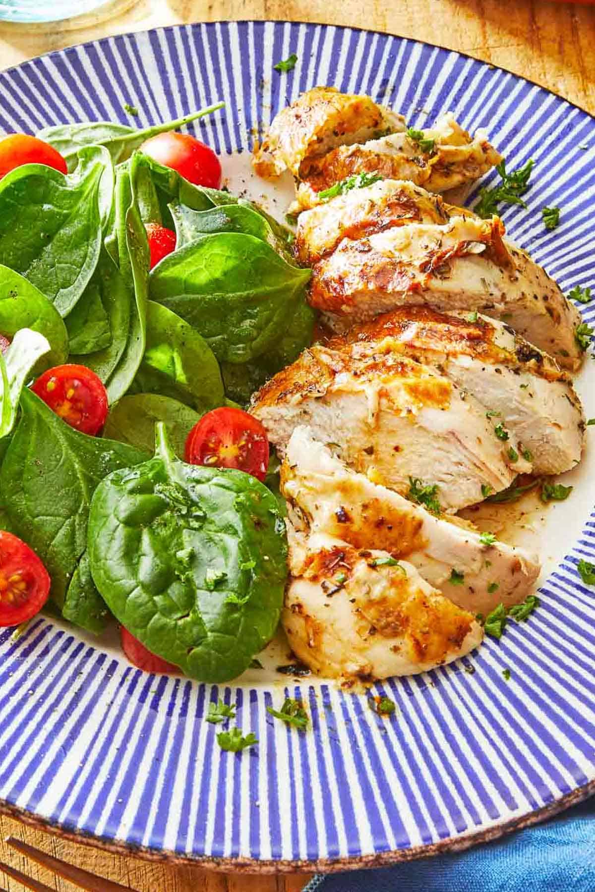 A piece of chicken sliced up on a plate with a spinach salad and cherry tomatoes.