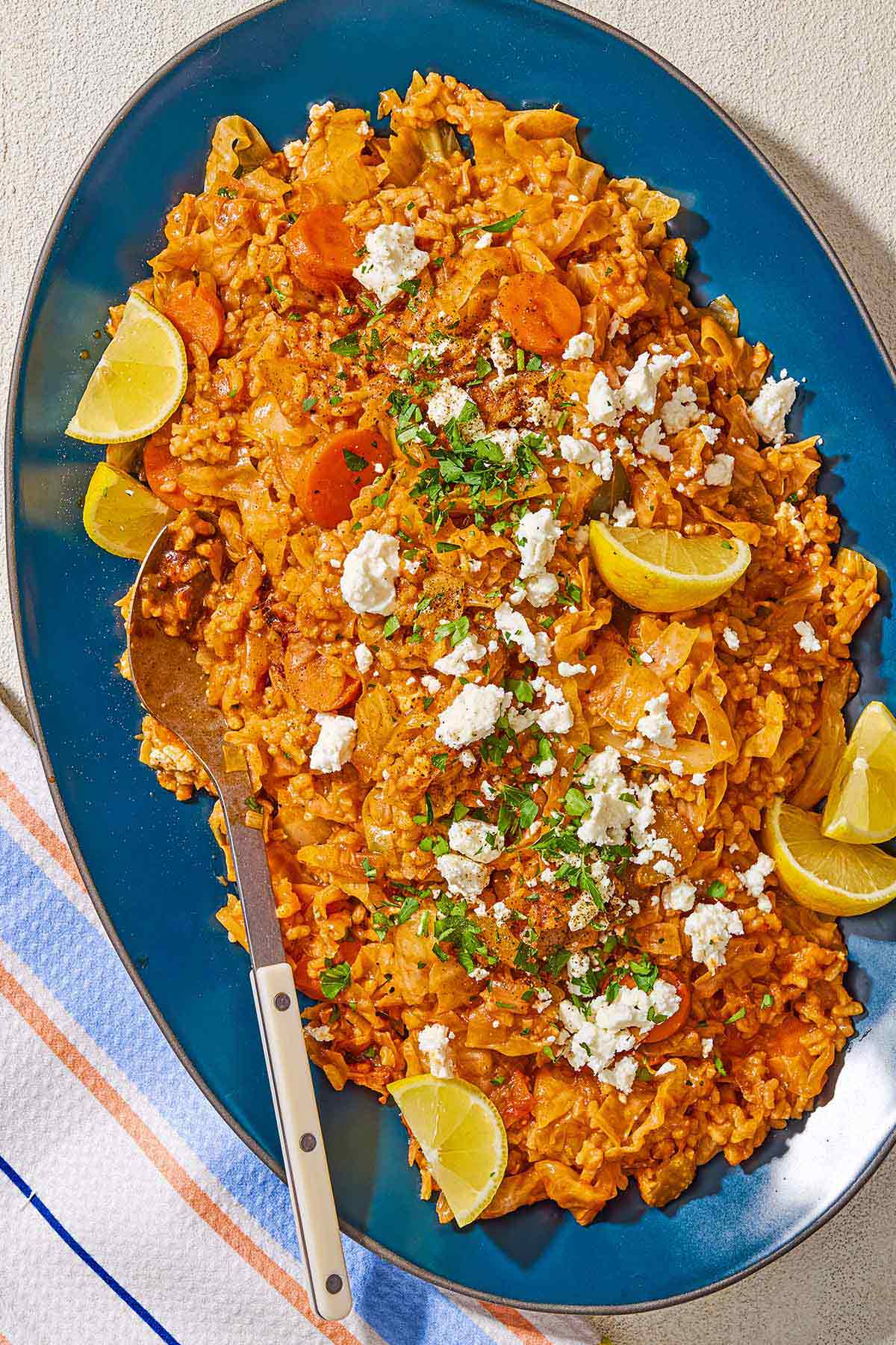 Greek cabbage rice topped with crumbled feta, chopped parsley and lemon wedges on a platter with a serving spoon.