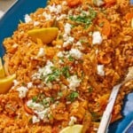 Greek cabbage rice topped with crumbled feta and chopped parsley on a platter with a serving spoon.