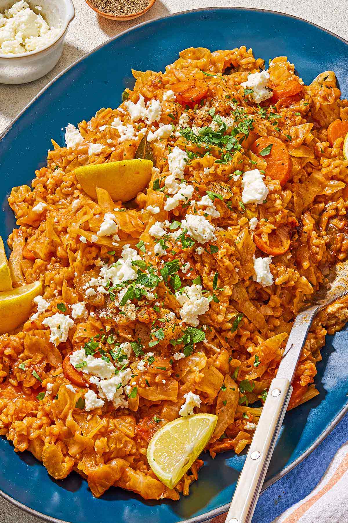 Greek cabbage rice topped with crumbled feta and chopped parsley on a platter with a serving spoon.