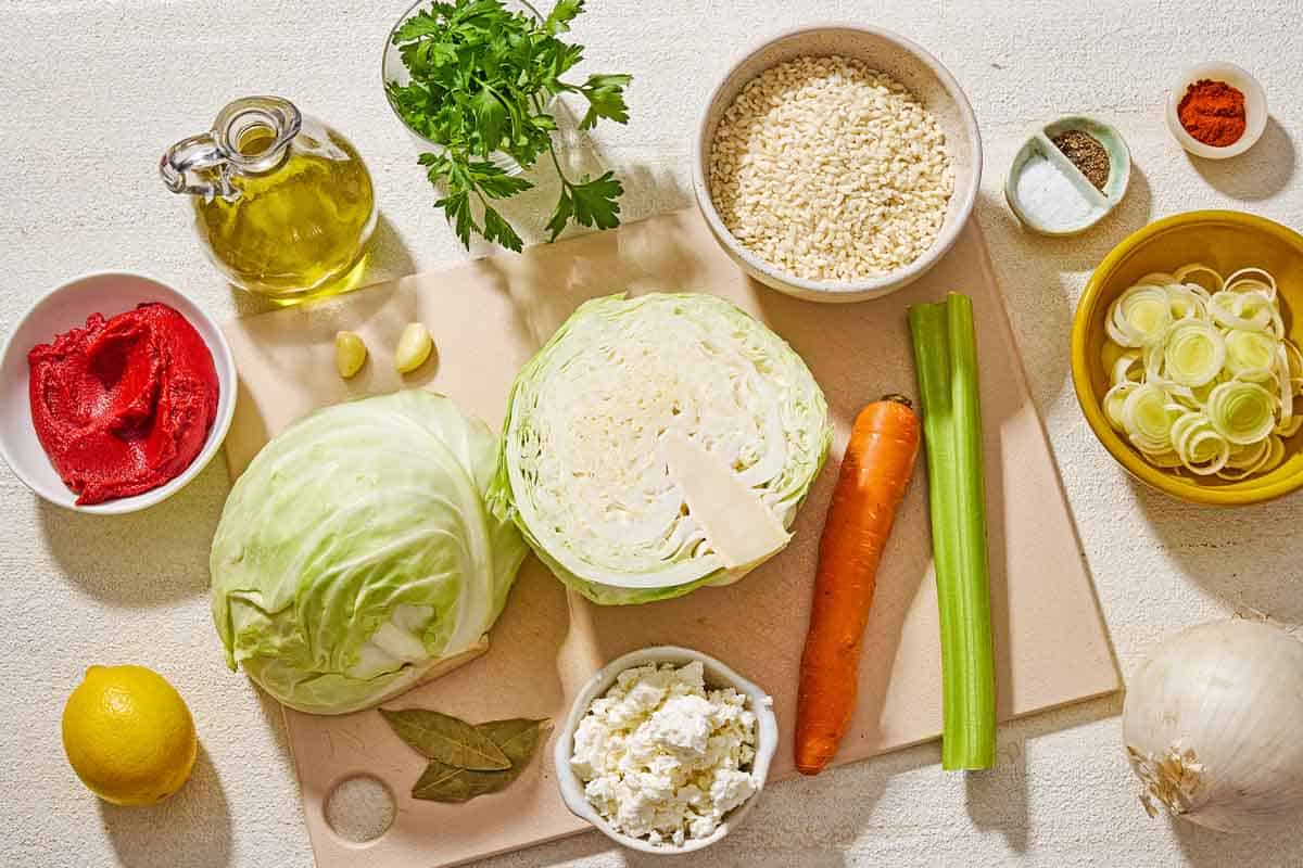 Ingredients for Greek cabbage rice including cabbage, olive oil, onion, a leek, a carrot, celery, salt, garlic, tomato paste, paprika, bay leaves, rice, black pepper, lemon, parsley and feta cheese.