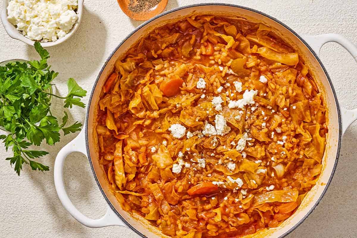 Greek cabbage rice topped with crumbled feta in a large pot next to a bunch of parsley and bowls of crumbled feta and black pepper.