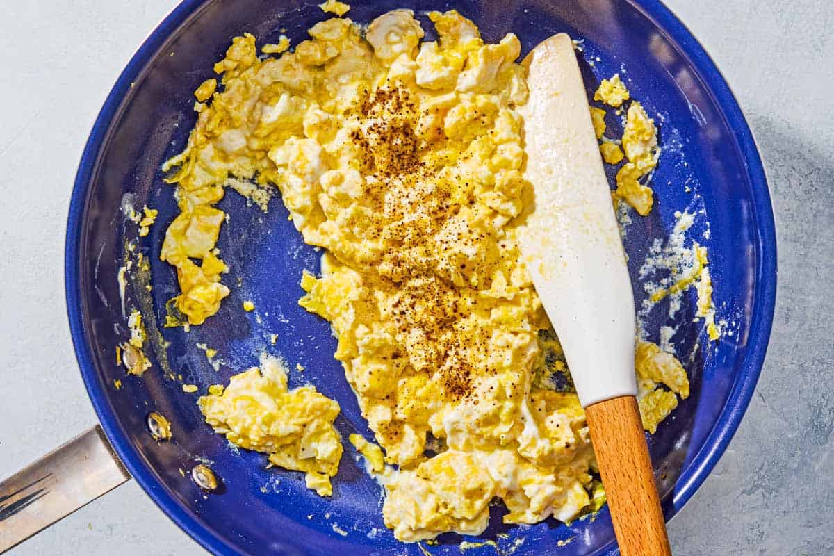 Scrambled eggs with sprinkled with salt and black pepper in a skillet with a spatula.