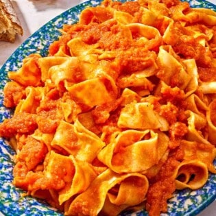 Pasta tossed with lentil bolognese on a platter next to a crusty baguette torn in half.