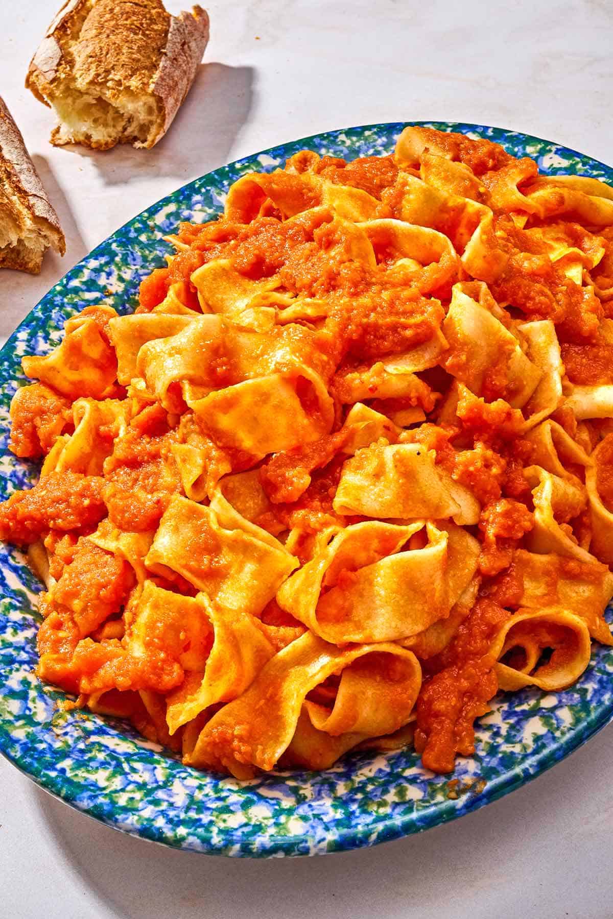 Pasta tossed with lentil bolognese on a platter next to a crusty baguette torn in half.