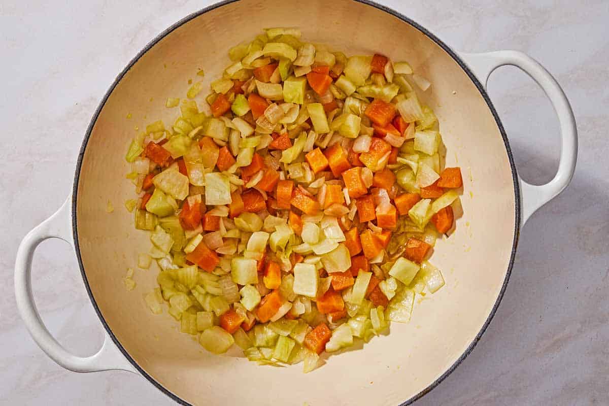 Sauteed chopped onion, carrot, and fennel in a pot.