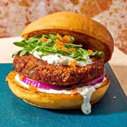 A vegetarian burger on a bun with yogurt herb sauce, red onion, grated carrots and arugula leaves.