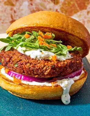 A vegetarian burger on a bun with yogurt herb sauce, red onion, grated carrots and arugula leaves.