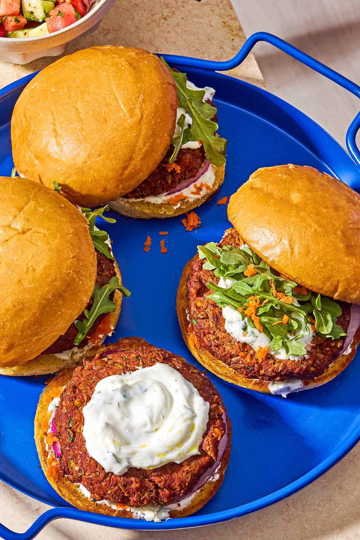 A try with 3 whole lentil burgers on buns, and a bun half with a lentil burger topped with yogurt herb sauce.