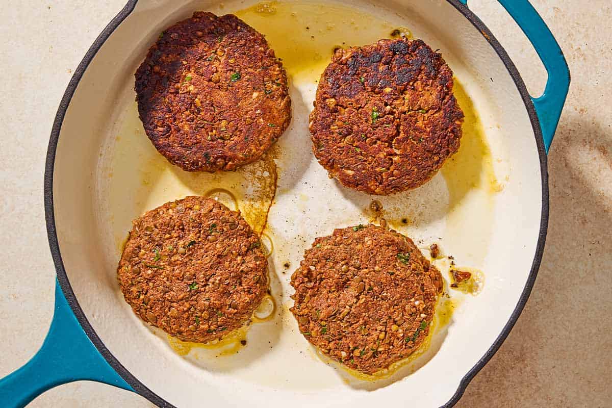 4 lentil burgers being cooked in a skillet.