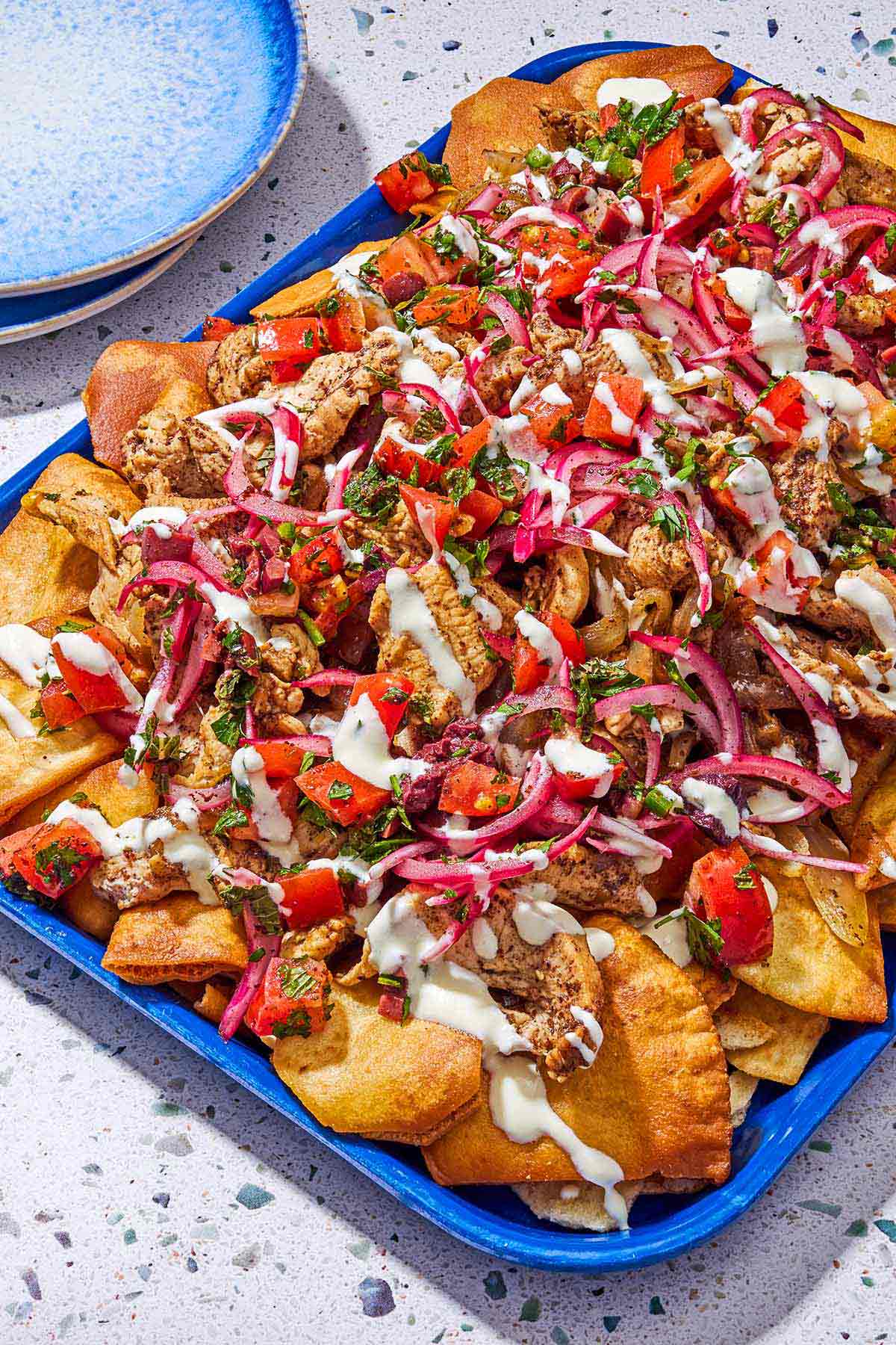 The chicken nachos on a platter next to a stack of 2 plates.