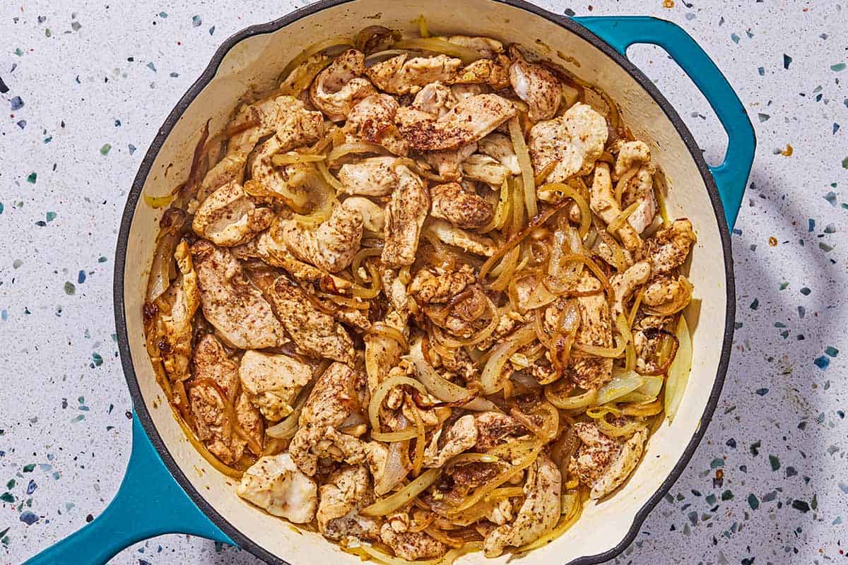 Sauteed chicken pieces and onions in a skillet.