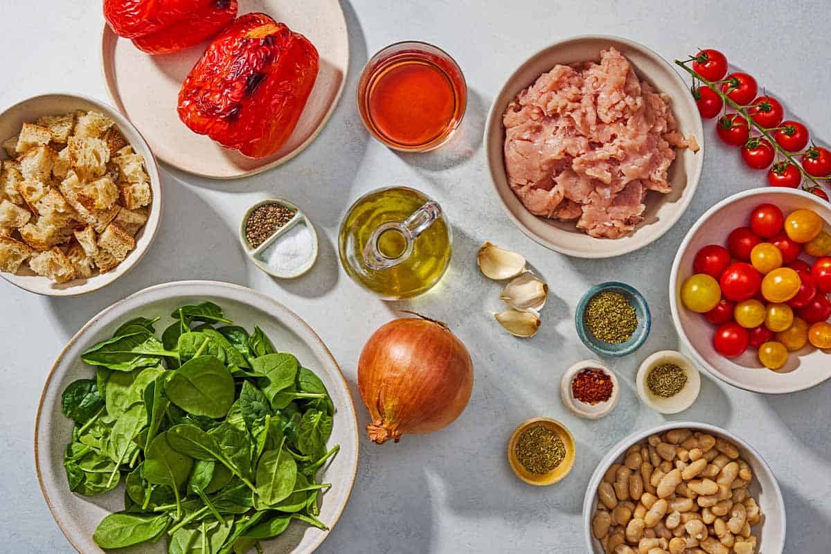 Ingredients for the ground turkey recipe including ground turkey, olive oil, salt, black pepper, cubed crusty bread, onion, garlic, ground fennel, oregano, thyme, aleppo pepper, baby spinach, cherry tomatoes, roasted red peppers, cannellini beans, and red wine vinegar.