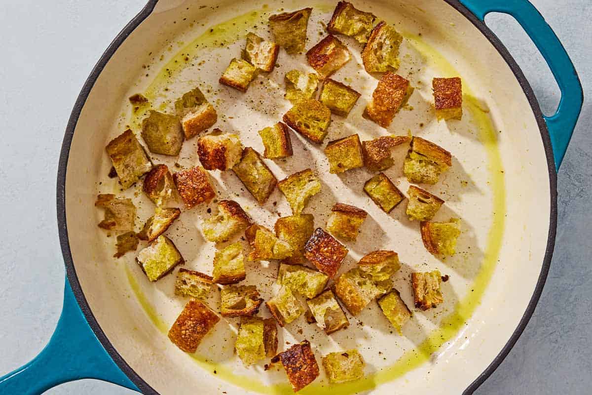 Cubes of crusty bread being toasted in olive oil in a skillet.