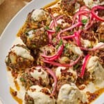 The turkish meatballs and yogurt sauce topped with pickled red onions and chopped parsley on a platter next to a bowl pickled red onions.