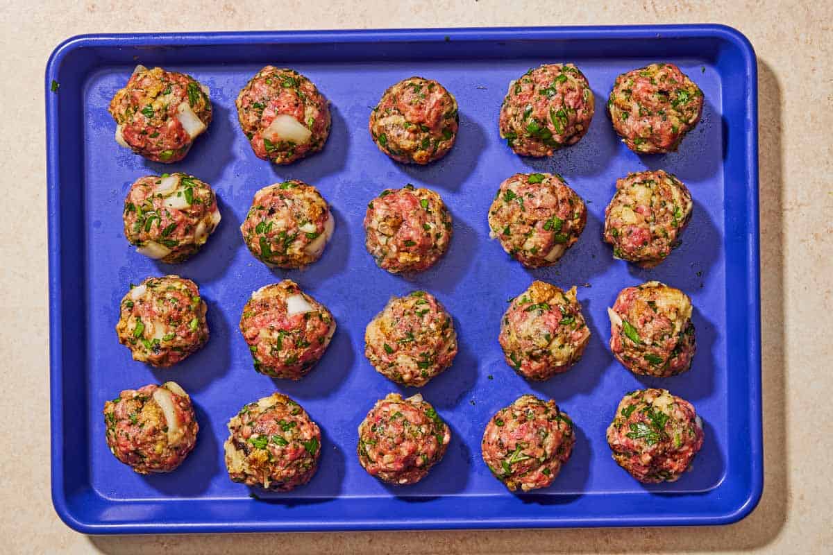 The unbaked turnkish meatballs spread evenly on a sheet pan.