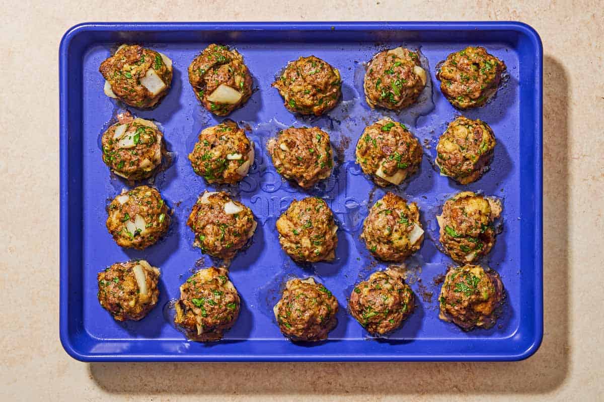 The baked turnkish meatballs spread evenly on a sheet pan.