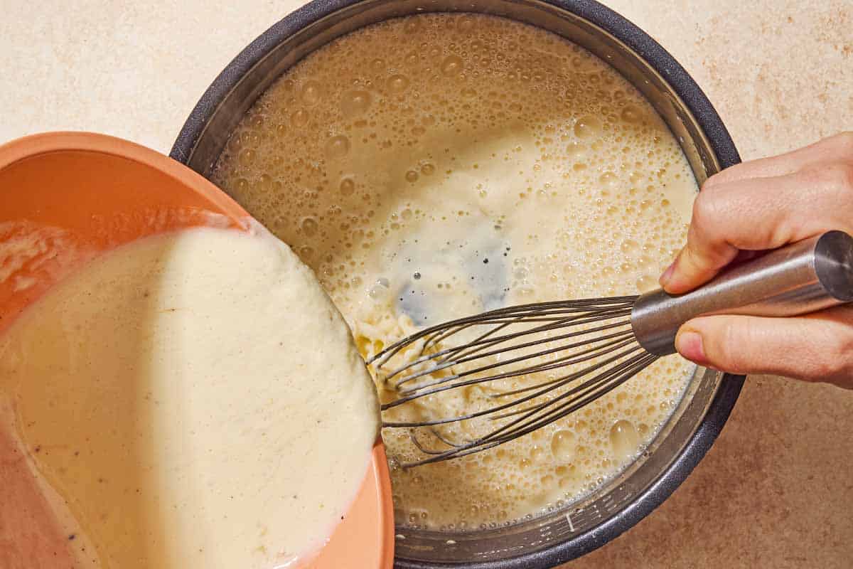 The yogurt sauce being poured from a bowl into a saucepan.