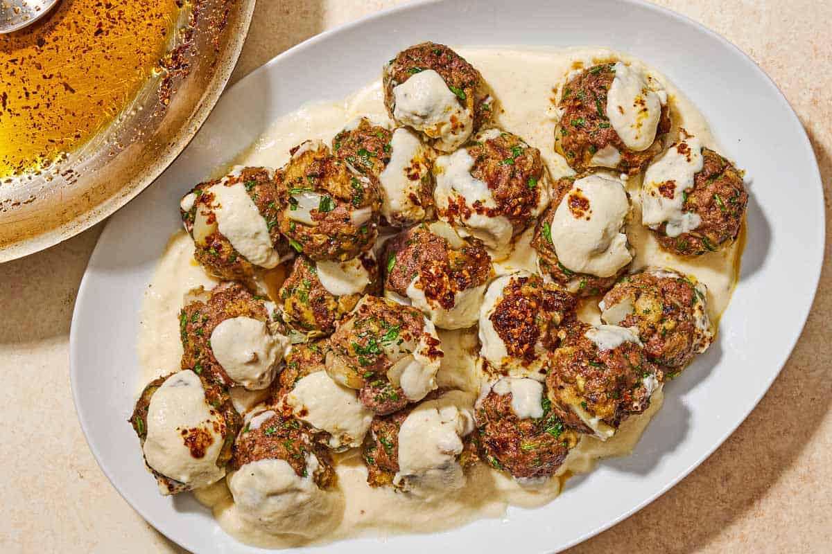 The turkish meatballs and yogurt sauce on a platter next to Aleppo pepper spiced olive oil in a skillet.