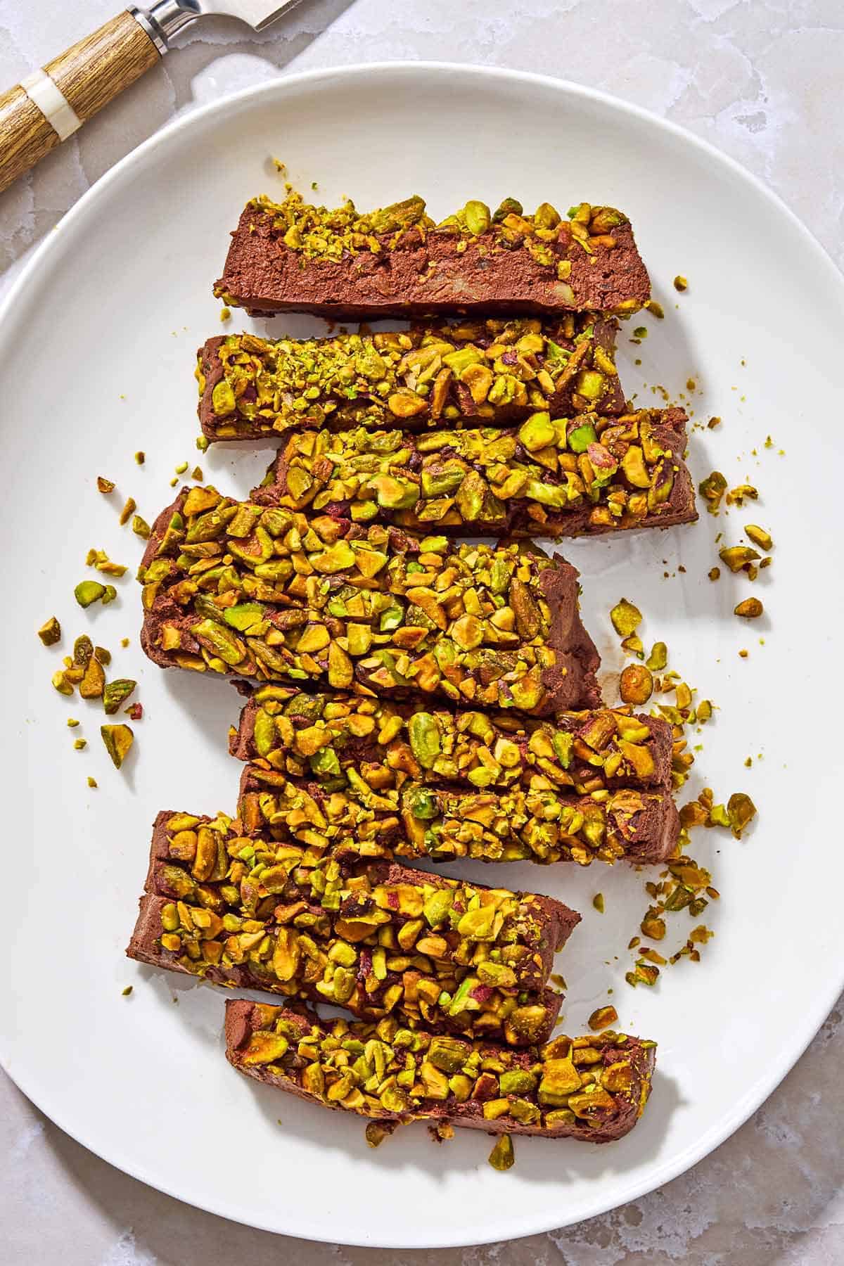 Sliced vegan chocolate mousse topped with pistachios on a white platter.