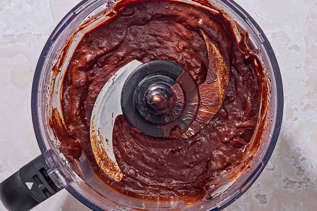 The apple and chocolate mixture in the bowl of a food processor fitted with a blade.