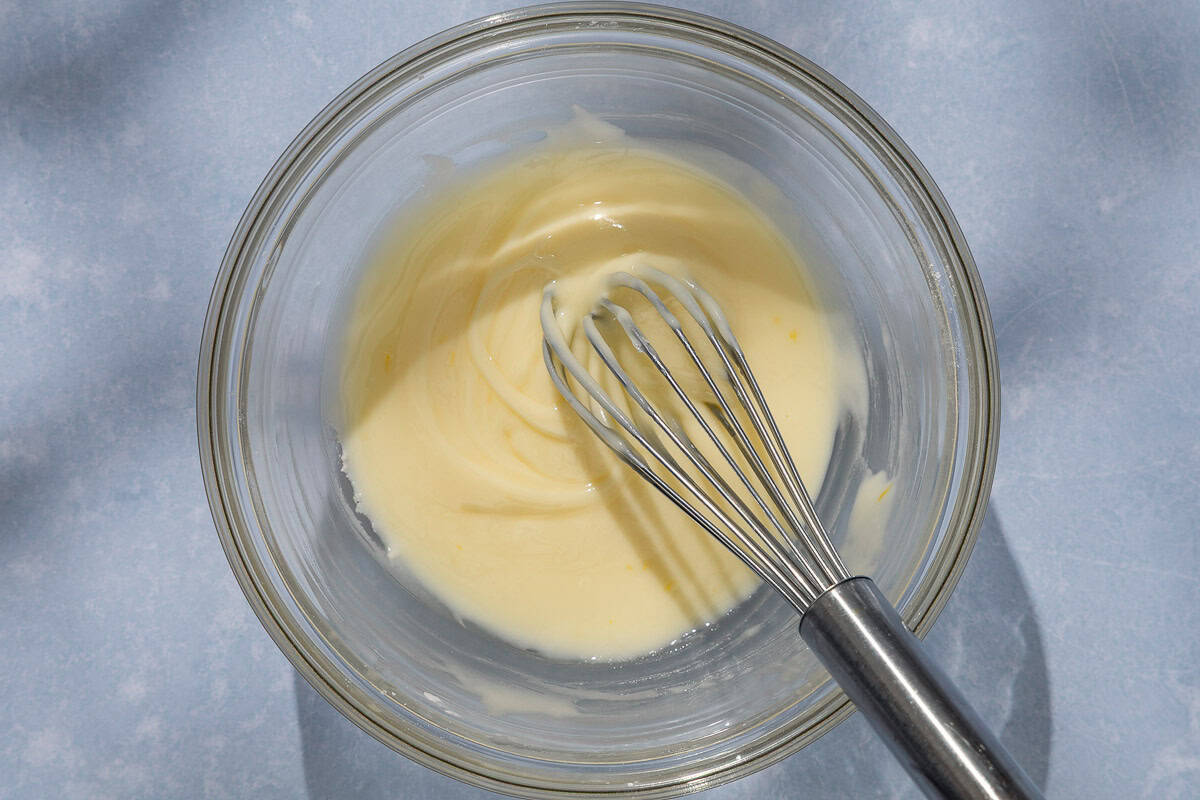 The glaze for the orange cake in a bowl with a whisk.