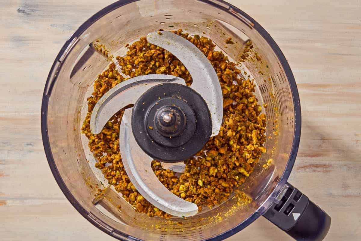 Finely chopped pistachios in the bowl of a food processor fitted with a blad.